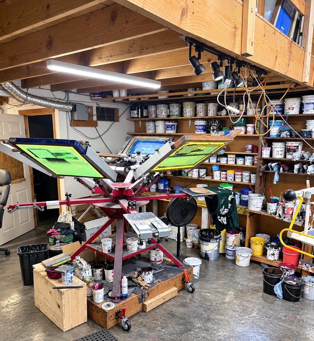 Manual press with green screens, surrounded by shelves of ink
